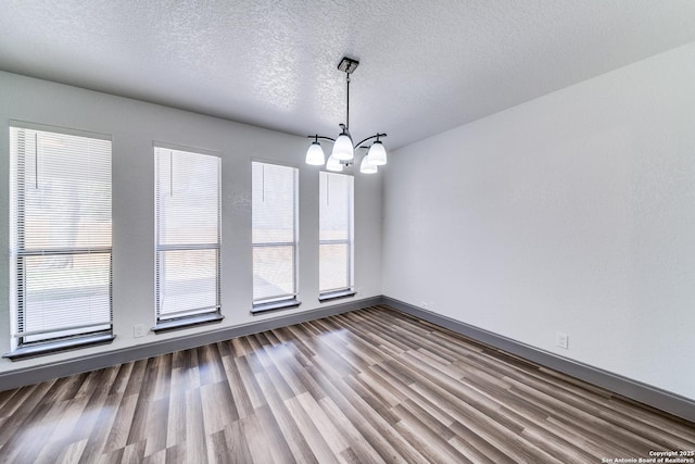 unfurnished dining area with wood-type flooring, a textured ceiling, and a notable chandelier