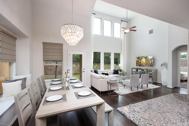 dining room with a high ceiling, ceiling fan with notable chandelier, and dark hardwood / wood-style flooring