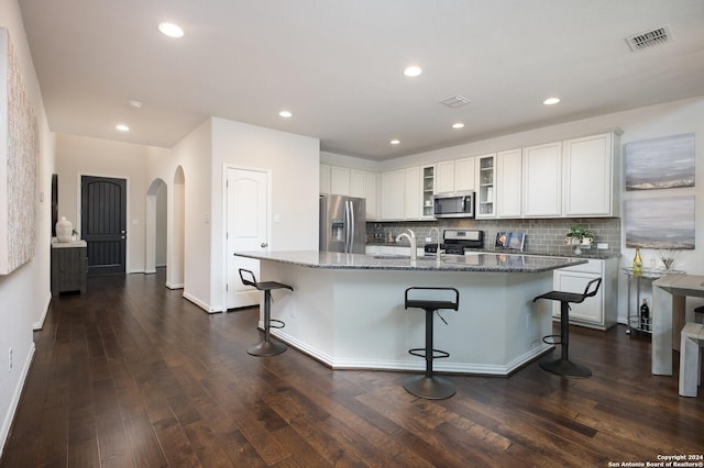 kitchen featuring a kitchen island with sink, a breakfast bar area, stainless steel appliances, and dark stone counters