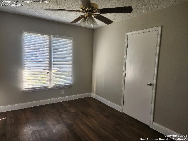 unfurnished room with a ceiling fan, a textured ceiling, baseboards, and dark wood-type flooring