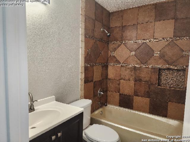 full bathroom featuring a textured wall, vanity, toilet, and shower / bathing tub combination