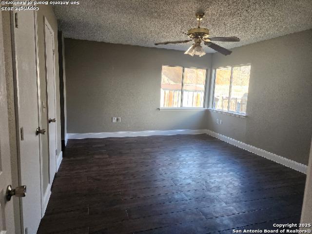 spare room with a textured ceiling, dark wood-type flooring, a ceiling fan, and baseboards