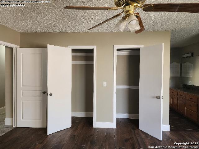 unfurnished bedroom featuring ceiling fan, dark hardwood / wood-style flooring, a textured ceiling, and two closets