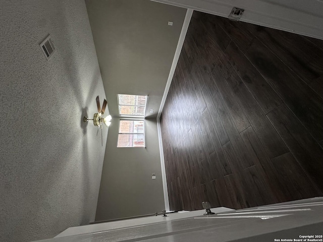 unfurnished room with dark wood-style flooring, visible vents, and a textured wall