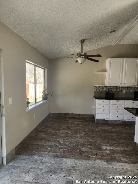 interior space with lofted ceiling, a textured ceiling, dark wood-type flooring, and white cabinets