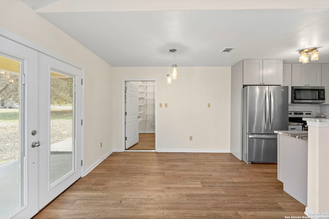 kitchen with stainless steel appliances, white cabinetry, hanging light fixtures, and light hardwood / wood-style flooring