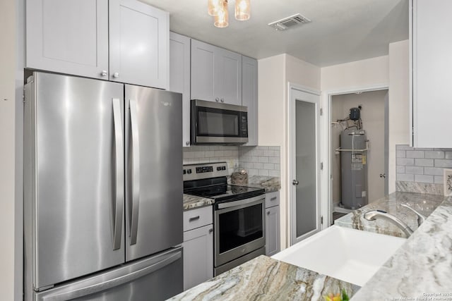 kitchen with appliances with stainless steel finishes, white cabinetry, sink, light stone countertops, and electric water heater