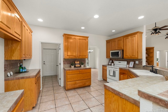 kitchen with tile countertops, sink, backsplash, ceiling fan, and white range with electric cooktop