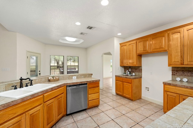 kitchen with sink, tasteful backsplash, light tile patterned floors, stainless steel dishwasher, and tile counters