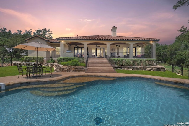 pool at dusk with ceiling fan and a patio