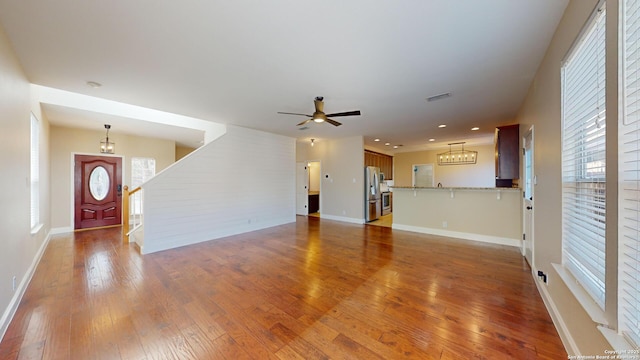 unfurnished living room with ceiling fan with notable chandelier and hardwood / wood-style floors