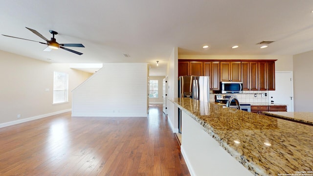 kitchen featuring light stone counters, ceiling fan, stainless steel appliances, light hardwood / wood-style floors, and decorative backsplash