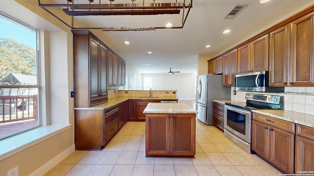 kitchen with light tile patterned flooring, a kitchen island, appliances with stainless steel finishes, kitchen peninsula, and light stone countertops