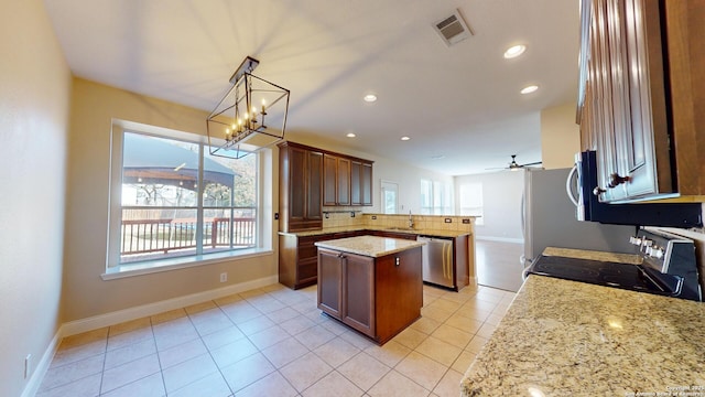 kitchen with a kitchen island, decorative light fixtures, decorative backsplash, stainless steel appliances, and light stone countertops