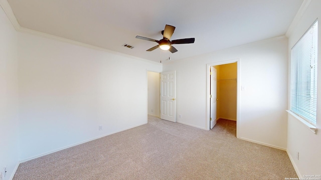 unfurnished bedroom featuring crown molding, ceiling fan, light carpet, a spacious closet, and a closet