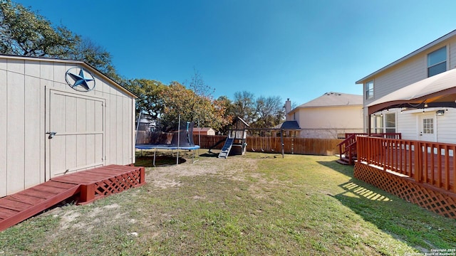 view of yard featuring a shed, a playground, a deck, and a trampoline