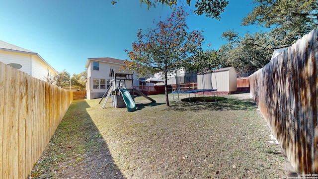 view of yard featuring a trampoline, a playground, and a storage unit