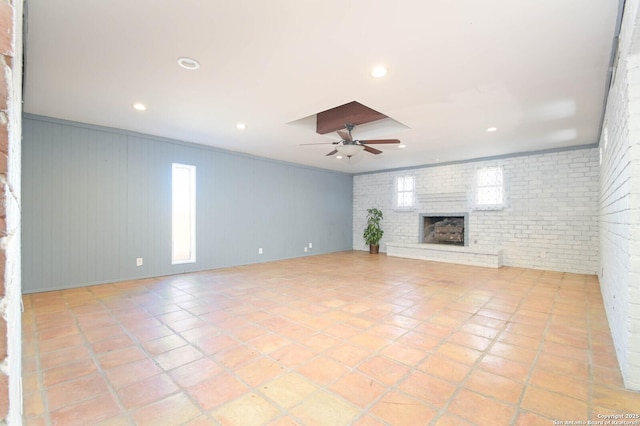 unfurnished living room with a brick fireplace, ceiling fan, a healthy amount of sunlight, and brick wall