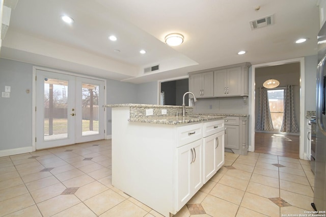 kitchen with light tile patterned flooring, sink, a kitchen island with sink, light stone countertops, and french doors