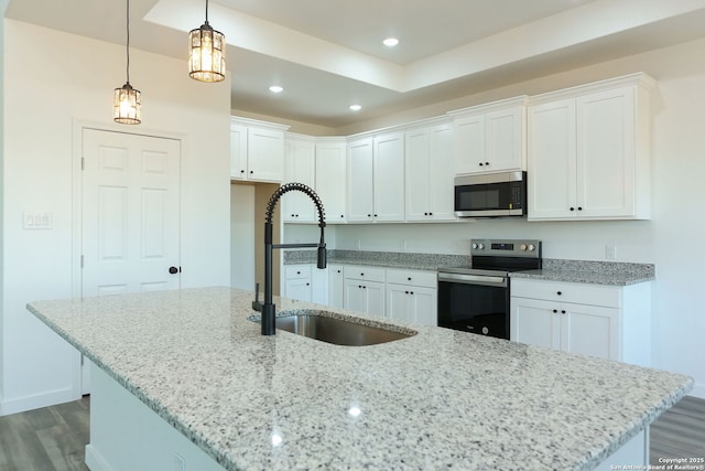 kitchen with sink, white cabinets, hanging light fixtures, stainless steel appliances, and a center island with sink