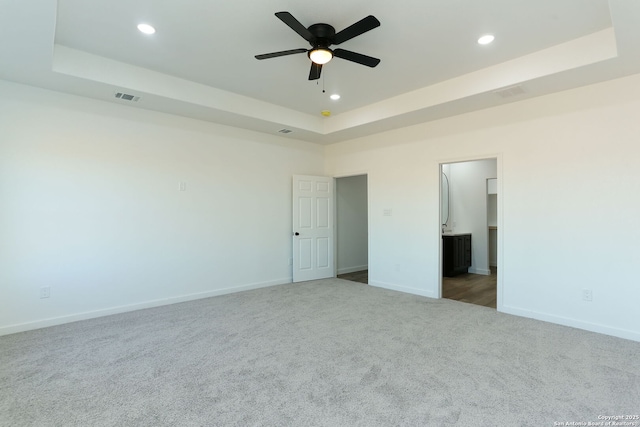 unfurnished bedroom featuring carpet flooring, a tray ceiling, and ensuite bath