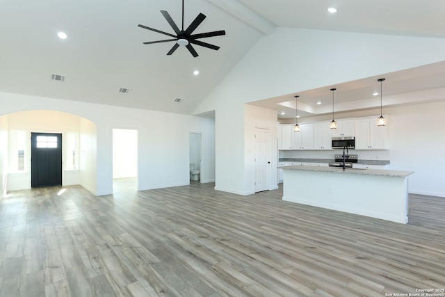 kitchen with pendant lighting, white cabinets, a kitchen island with sink, light stone counters, and light hardwood / wood-style flooring