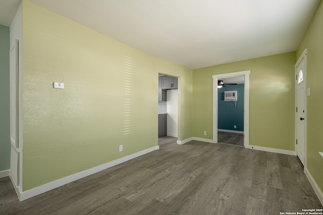 spare room with dark wood-type flooring, a wall unit AC, and ceiling fan