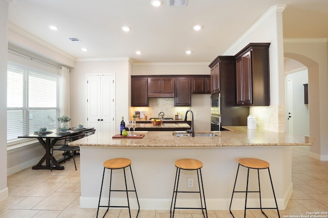 kitchen with sink, a kitchen breakfast bar, light stone counters, ornamental molding, and kitchen peninsula