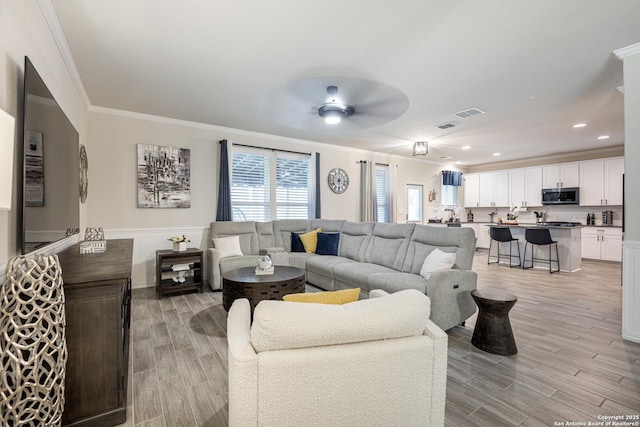 living room featuring light hardwood / wood-style flooring, ornamental molding, and ceiling fan