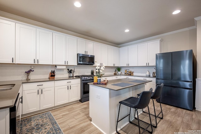 kitchen featuring black refrigerator, ornamental molding, range with gas stovetop, a kitchen island, and white cabinets