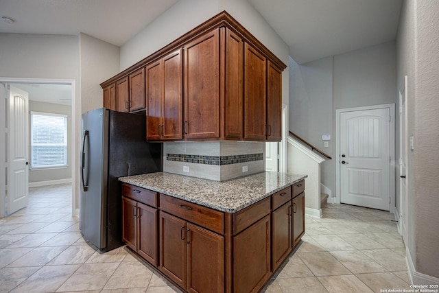 kitchen with light tile patterned flooring, light stone countertops, stainless steel fridge, and backsplash