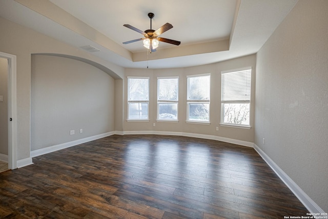 empty room with dark hardwood / wood-style flooring, a tray ceiling, and ceiling fan