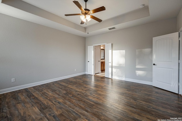 unfurnished bedroom featuring a tray ceiling, dark wood-type flooring, and ceiling fan