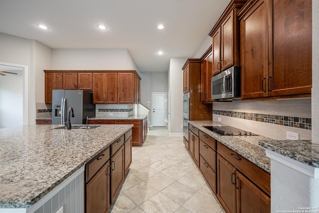 kitchen featuring sink, decorative backsplash, a kitchen island with sink, light stone counters, and stainless steel appliances