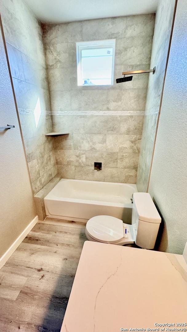 bathroom with hardwood / wood-style floors, tiled shower / bath, and toilet