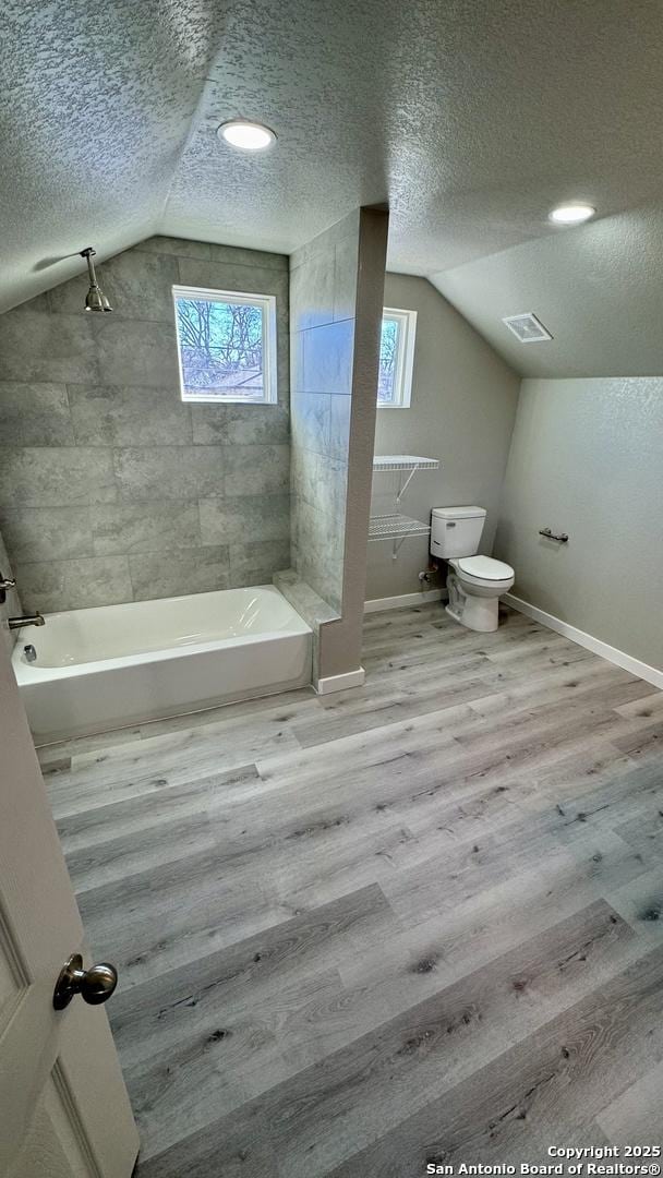 bathroom with hardwood / wood-style floors, tiled shower / bath, and a textured ceiling