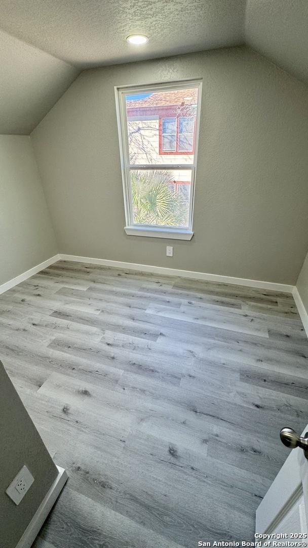 additional living space with vaulted ceiling, light wood-type flooring, and a textured ceiling