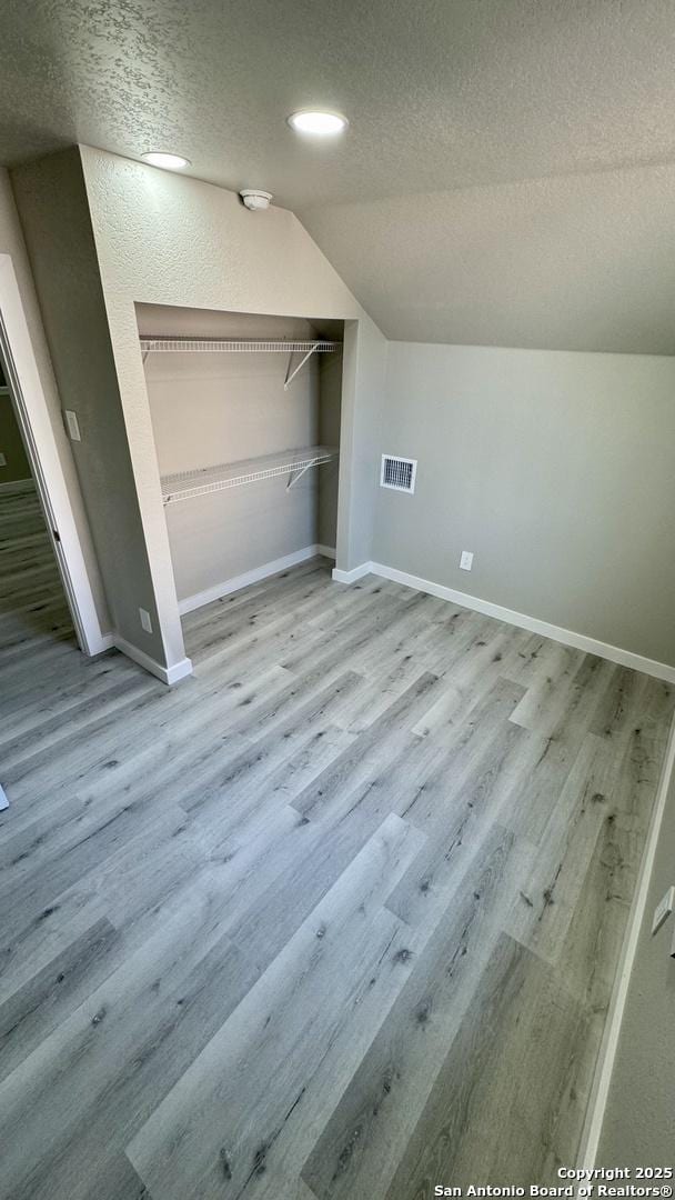 bonus room with lofted ceiling, a textured ceiling, and light wood-type flooring