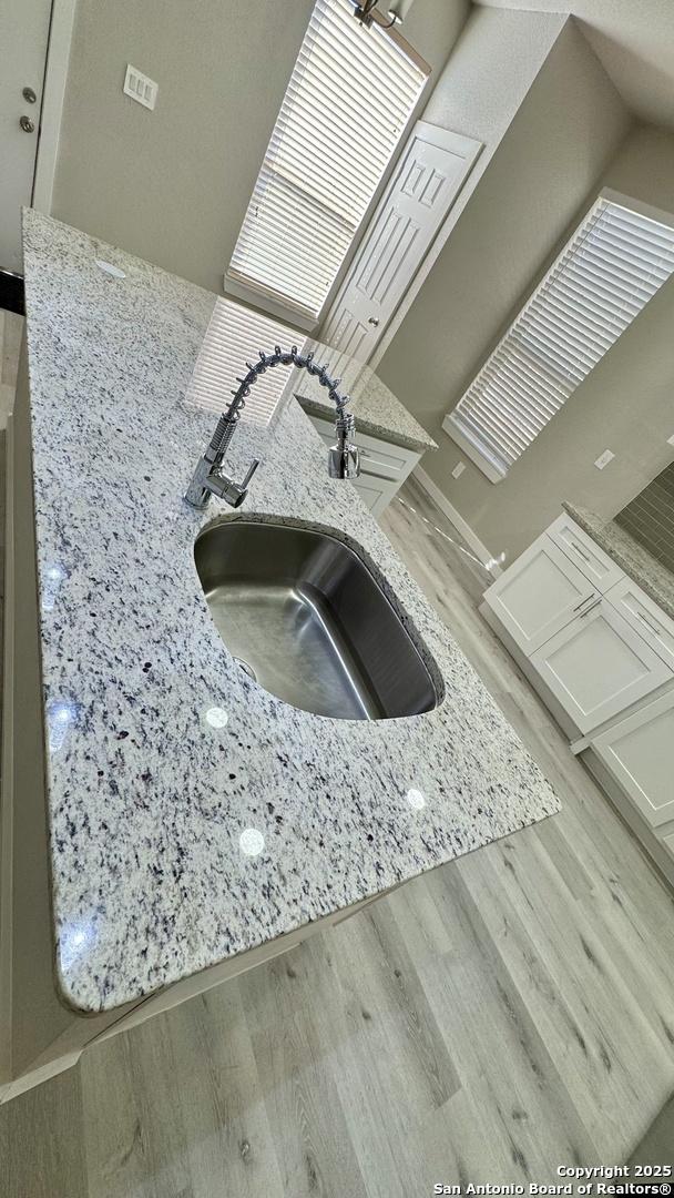 interior details featuring white cabinetry, light hardwood / wood-style floors, light stone countertops, and sink