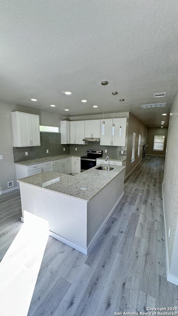 kitchen featuring sink, stainless steel range with electric stovetop, pendant lighting, light hardwood / wood-style floors, and white cabinets