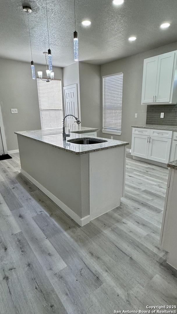 kitchen with white cabinetry, decorative light fixtures, an island with sink, and light wood-type flooring