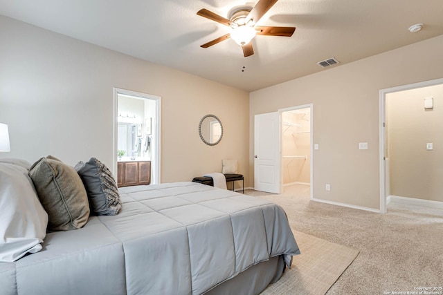 bedroom with connected bathroom, a spacious closet, light colored carpet, and ceiling fan