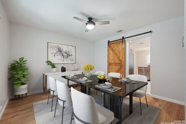 dining area with ceiling fan, a barn door, and light wood-type flooring