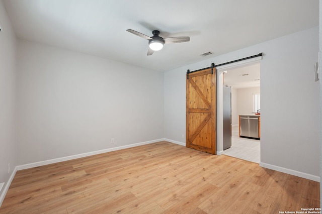 unfurnished room with ceiling fan, a barn door, and light hardwood / wood-style floors