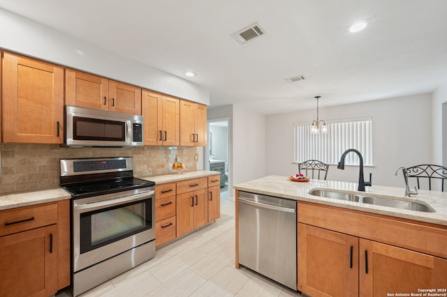 kitchen with sink, backsplash, hanging light fixtures, light stone counters, and stainless steel appliances