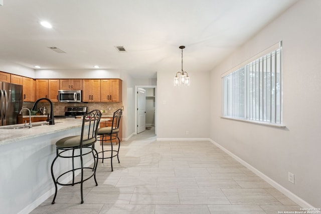 kitchen featuring appliances with stainless steel finishes, decorative light fixtures, sink, backsplash, and a kitchen bar