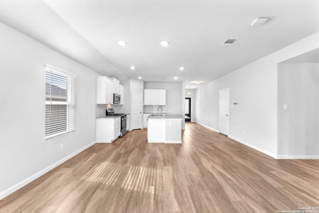 kitchen featuring appliances with stainless steel finishes, a center island with sink, white cabinets, and light hardwood / wood-style floors