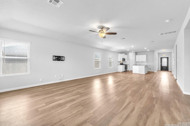 unfurnished living room featuring sink, a textured ceiling, ceiling fan, and light wood-type flooring