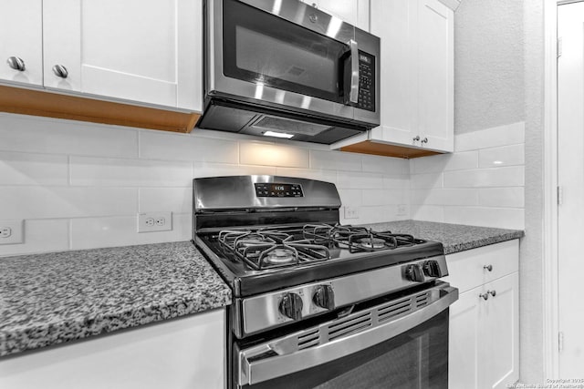 kitchen with stainless steel appliances, dark stone countertops, white cabinets, and backsplash