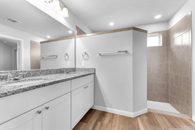 bathroom featuring vanity, tiled shower, hardwood / wood-style floors, and a textured ceiling